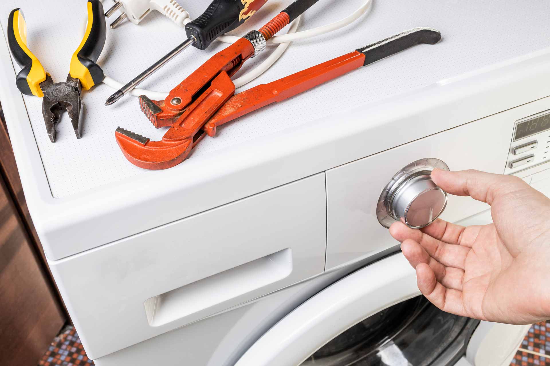 Wrench, pliers, and other tools sitting on top of a washer/dryer